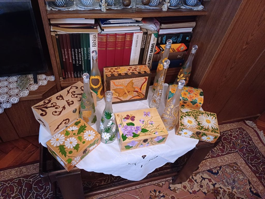 Lilian-Radovi-03 Stolić prekriven raznobojno oslikanim kutijicama i bocama Lilian Čuljak
